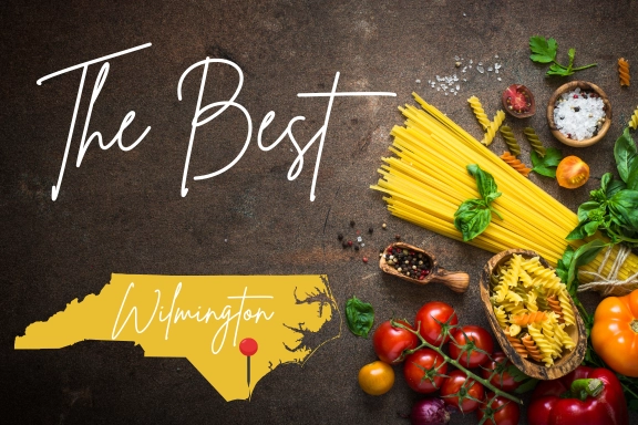 A variety of pasta, herbs, and tomatoes on a dark surface, with text reading The Best and an outline of North Carolina showing Wilmington, marked by a red dot—capturing the fresh ingredients inspired by the best restaurants in Wilmington NC.
