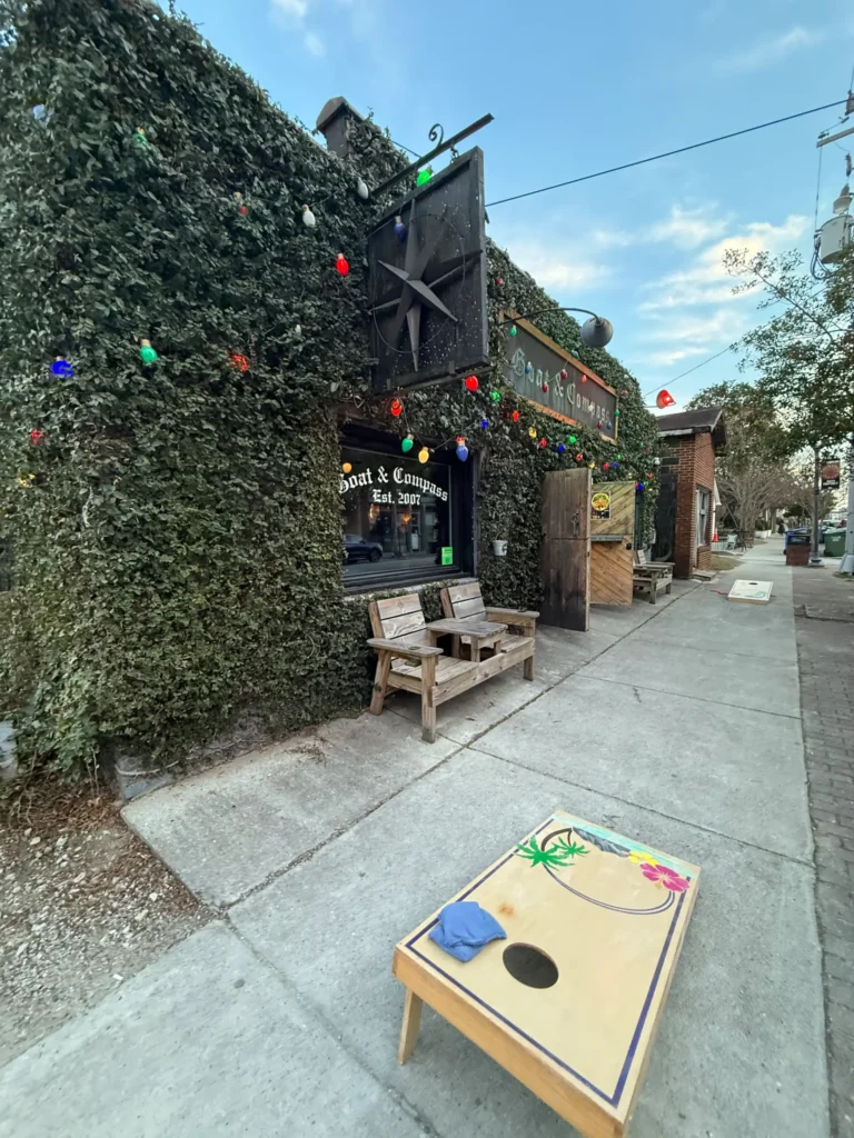 A small ivy-covered building with a large metal star sign, string lights, and a bench outside; a cornhole game board sits on the sidewalk in front—one of Wilmington NC's charming local finds tucked within vibrant neighborhoods.
