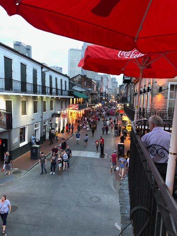 A view from a balcony looking down onto the crowded Bourbon Street at dusk, framed by a red Coca-Cola umbrella.