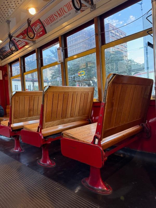 Empty wooden bench seats inside a New Orleans streetcar, perfect for a travel guide, with city views visible through the windows.